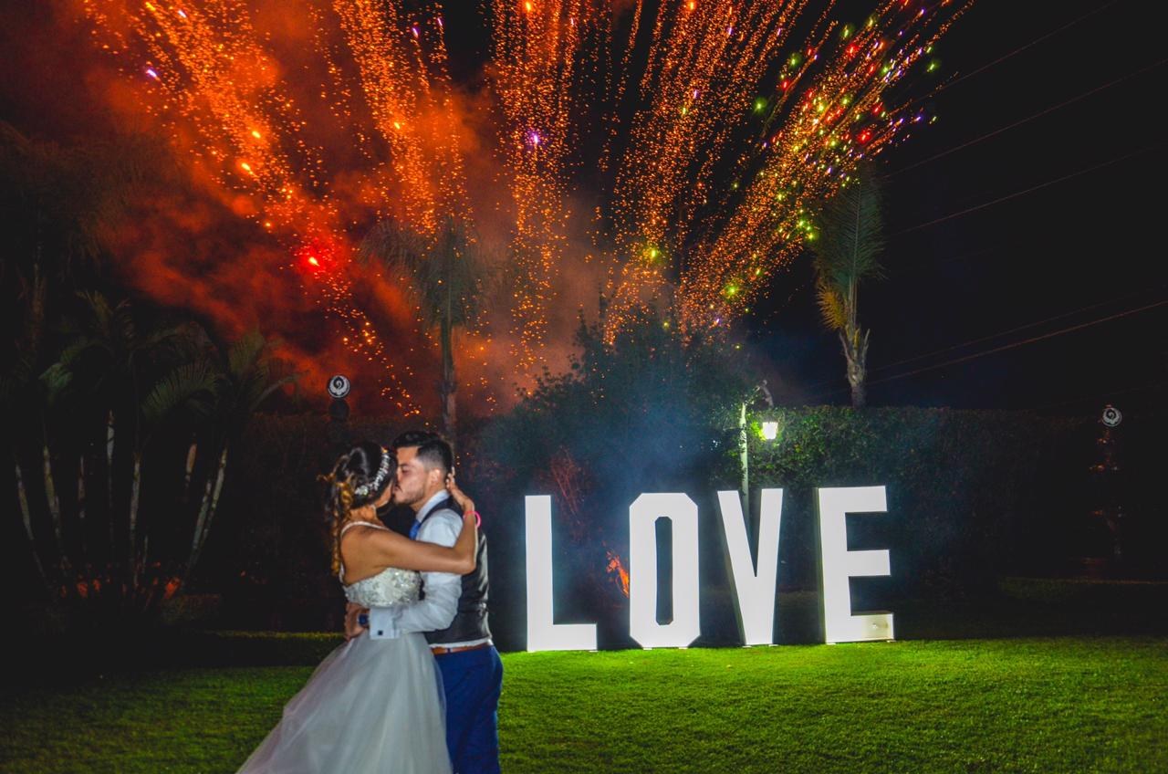 Pareja junto a letras LOVE y fuegos artificiales